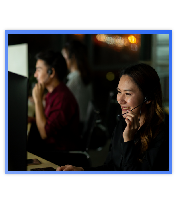 Woman talking on headset looking at computer with man in the background doing the same